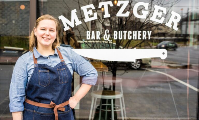 Metzger Bar and Butchery owner Brittanny Anderson stands outside her restaurant, wearing denim dungarees and a blue top.