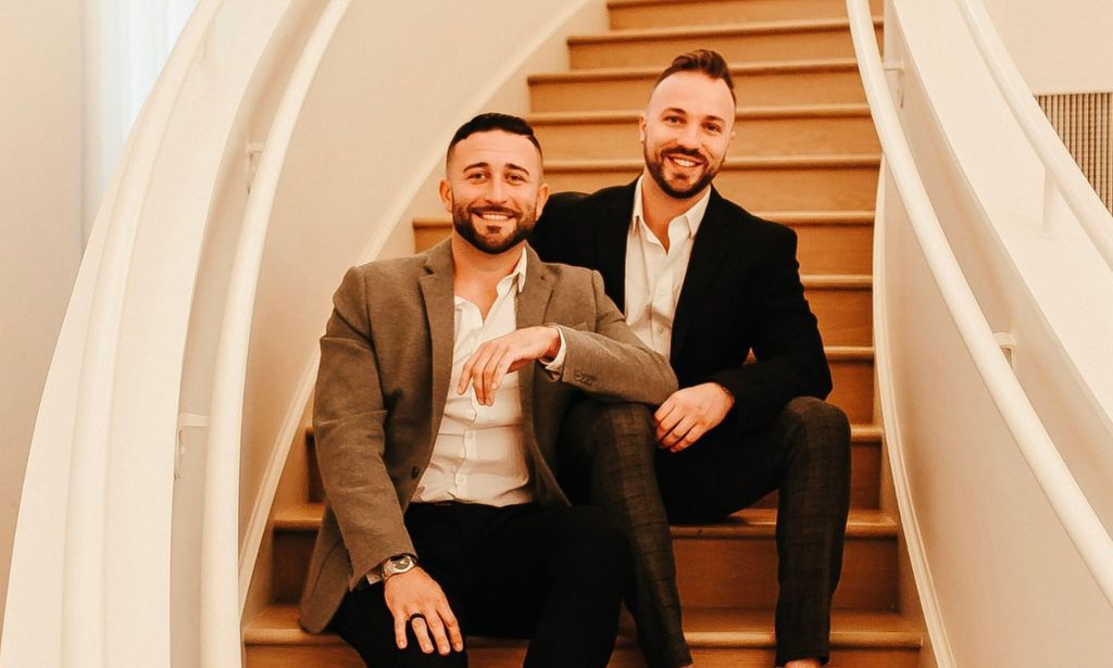 TJ House et Ryan Neitzel sont assis ensemble sur des escaliers en bois incurvés, s'appuyant affectueusement l'un sur l'autre.
