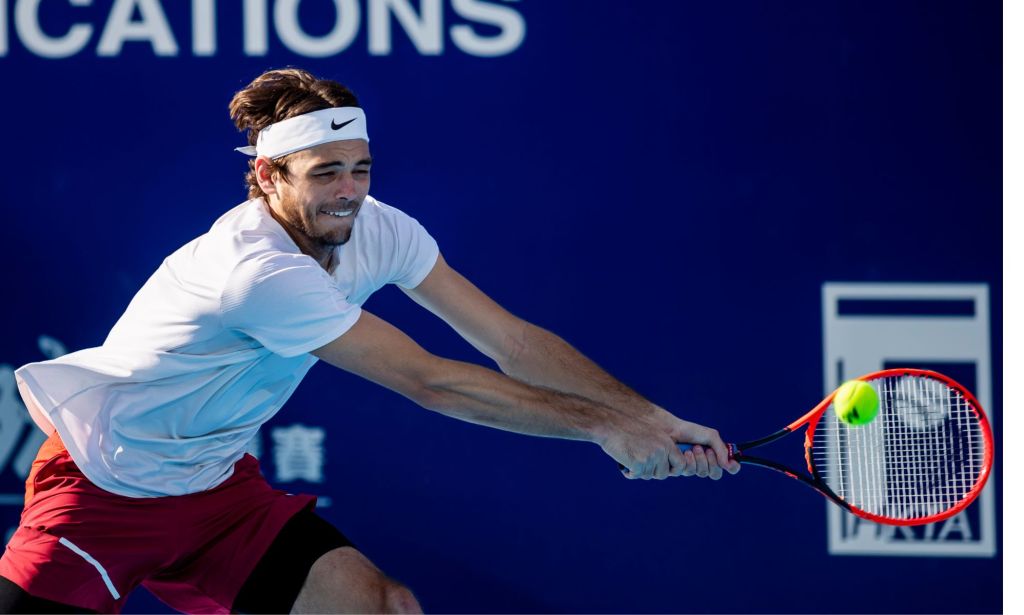 Taylor Fritz, vêtu d'un haut blanc, se précipite sur une balle de tennis avec une raquette rouge à la main lors d'un match ATP.