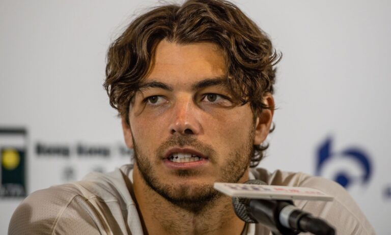 Taylor Fritz, wearing a white tee, speaks during a press conference into a small microphone.