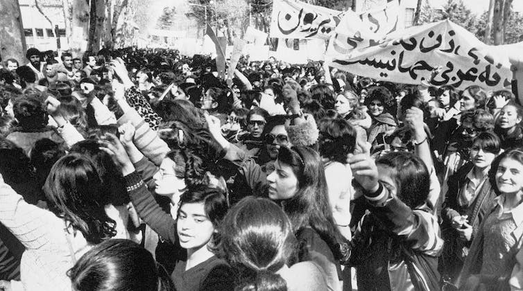 Une photo en noir et blanc montrant des centaines de jeunes filles marchant en procession et brandissant des banderoles.