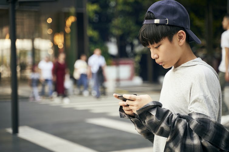 Garçon en casquette de baseball regardant son téléphone à l'extérieur au coin de la rue.