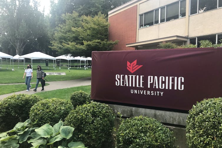 Deux étudiants marchent sur un trottoir près d'un panneau indiquant 