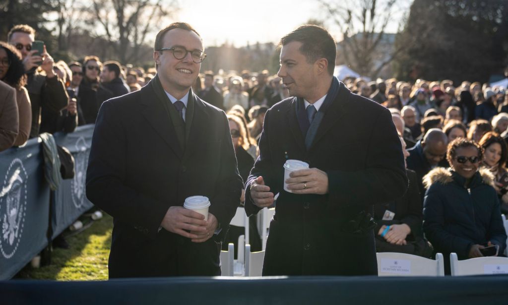 Pete et Chasten Buttigieg, tous deux vêtus de costumes noirs, discutent avec un groupe de personnes assises.