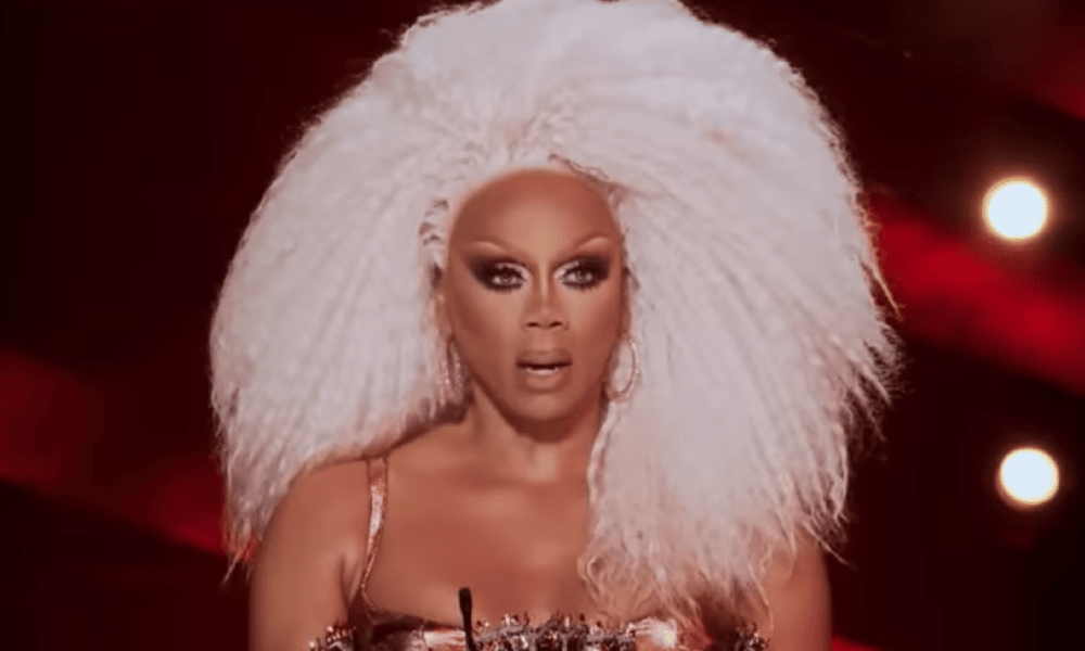 RuPaul avec de grands cheveux blonds, l'air choqué