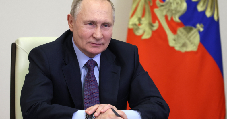 Le président russe Vladimir Poutine est assis à un bureau à côté d'un drapeau avec un stylo à la main.