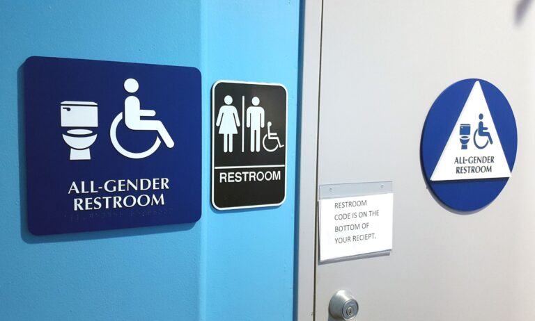 Signs on a wall show members of the public that the bathroom is an 'all gender restroom' and inclusive of trans people