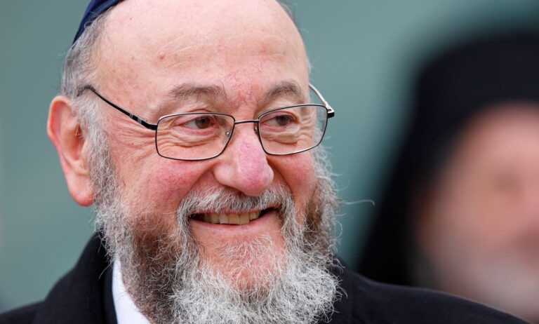 Ephraim Mirvis smiles as he looks off to the left, wearing a black coat.