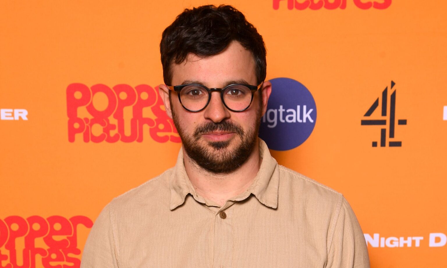 La star d’Inbetweeners dit que l’émission n’aurait pas lieu aujourd’hui à cause, vous savez, de toute l’homophobie endémique Simon Bird, wearing a cream top, smiles against an orange backdrop.