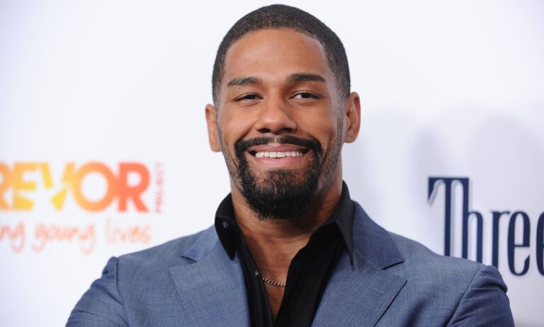 A photo showing professional wrestler Fred Rosser wearing a light blue suit jacket and black shirt smiling to the camera while on the red carpet.