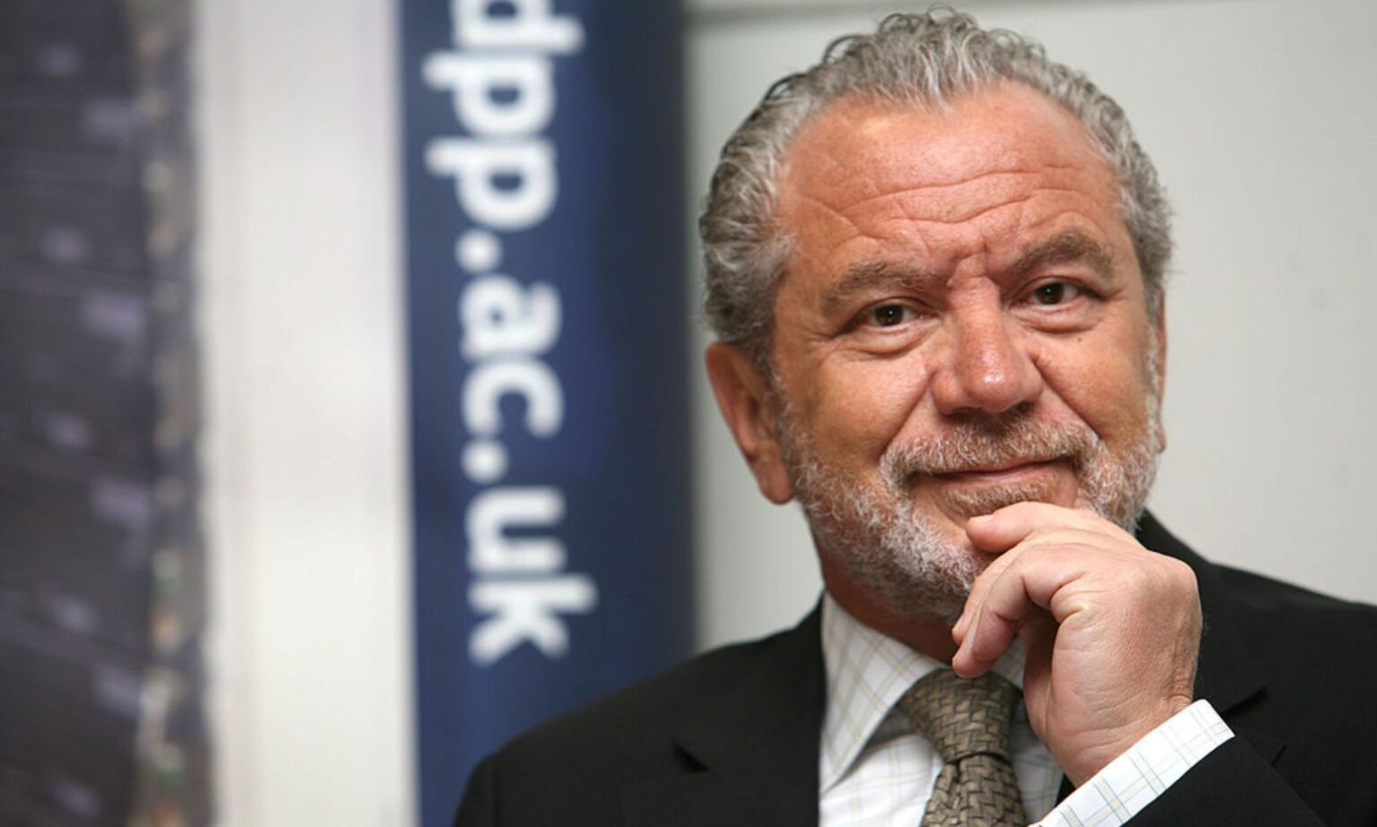 Alan Sugar intervient dans l’histoire d’EastEnders sur le VIH et passe à côté d’un point flagrant Alan Sugar in a promotional image. He is seen wearing a dark suit and tie.