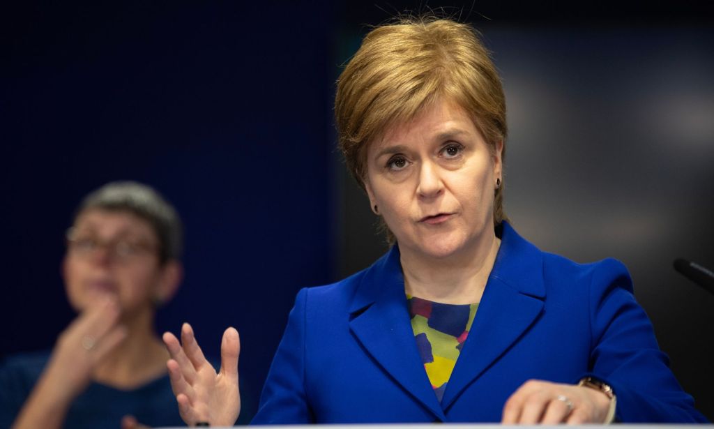 La première ministre écossaise Nicola Sturgeon porte une veste bleue alors qu'elle se tient sur un podium lors d'une conférence de presse