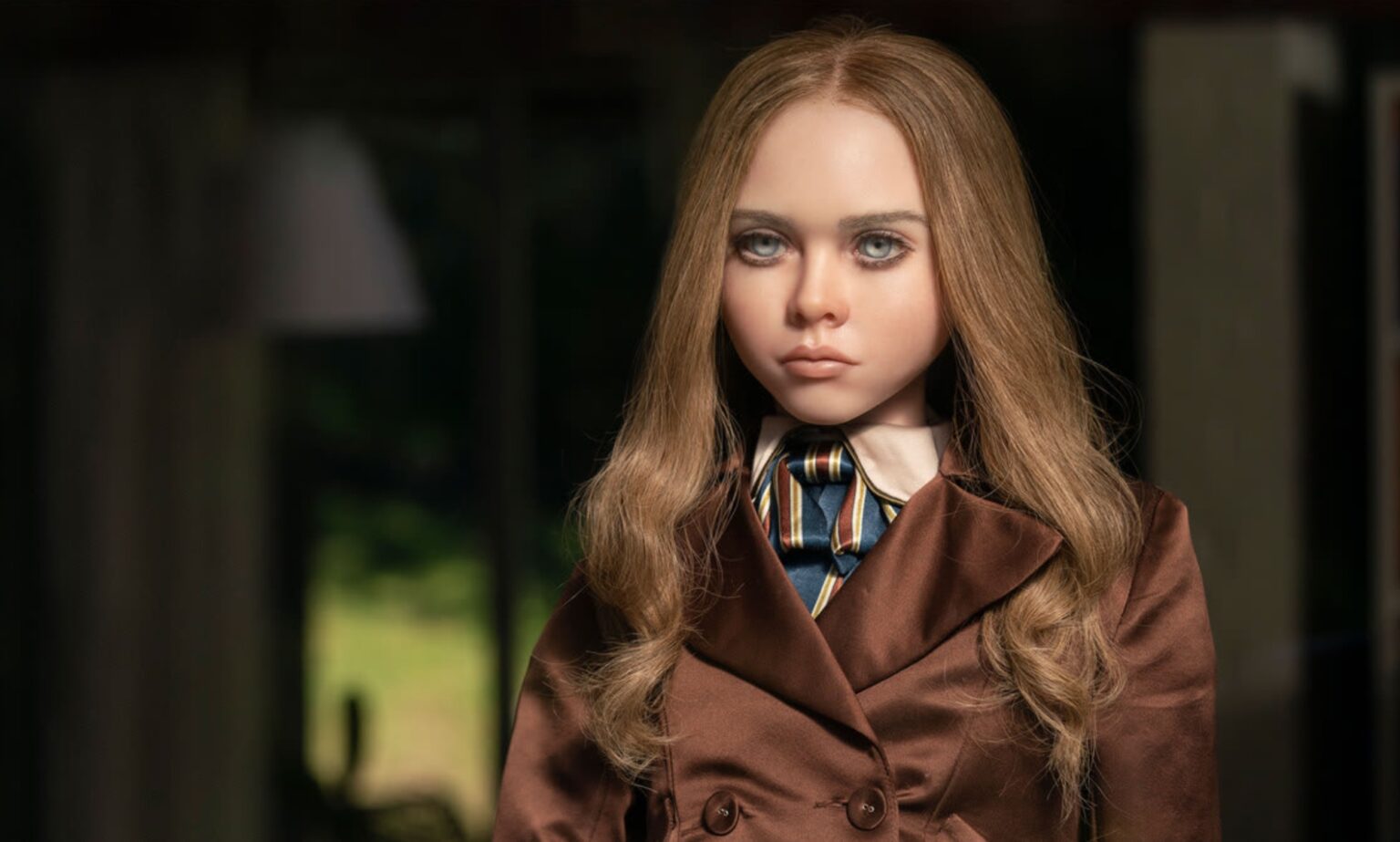 M3GAN revient officiellement pour une suite et les fans ont plein d’idées : « Je veux qu’elle combatte Chucky » A still from the movie M3GAN shows the AI doll dressed in a brown coat looking out of a window.