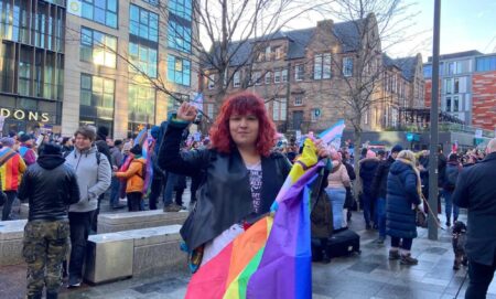 One of the protesters, a white woman with red hair holding a Pride flag, in front of a crowd of others