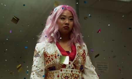 A screenshot from the movie Everything Everywhere All at Once shows actor Stephanie Hsu as character Joy who's dressed in a white and red oriental-style outfit with her hair dyed pink.