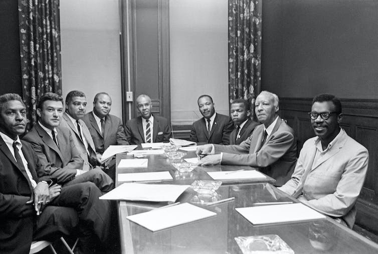 Un groupe d'hommes est assis autour d'une grande table avec des feuilles de papier devant eux.