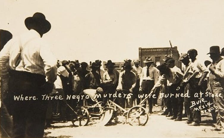 Des dizaines d'hommes portant des chapeaux ont la tête baissée alors qu'ils regardent le site où trois hommes noirs ont été brûlés sur le bûcher.