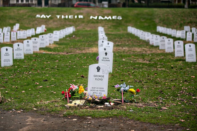 La pierre tombale de George Floyd se trouve au premier plan dans un faux cimetière ordonné avec d'autres pierres tombales blanches installées dans l'herbe