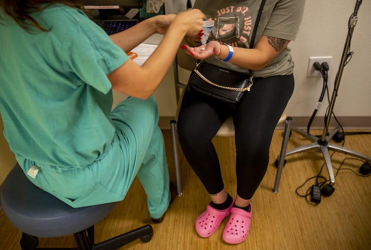 Une femme en gommage donne une pilule à une femme en leggings noirs et Crocs roses