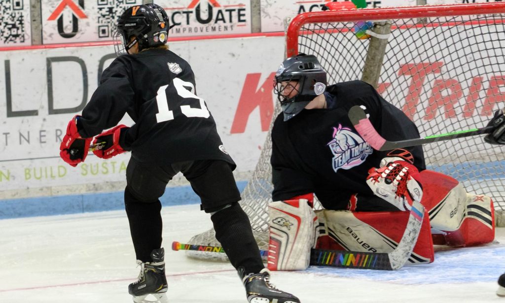 Un joueur de hockey de l'équipe Trans s'approche du but sur patins tandis que le gardien de but est posé sur la glace devant le but