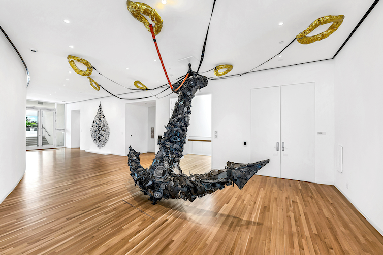 Une grande ancre sculptée au centre d'une galerie d'art, avec des liens vers des gilets de sauvetage montés au plafond.