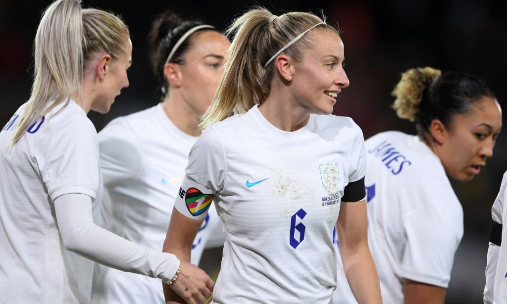 La capitaine des Lionnes Leah Williamson se tient aux côtés de ses coéquipières de football tout en portant un uniforme blanc et un brassard arc-en-ciel OneLove