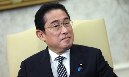 Japan’s prime minister Fumio Kishida wears a white shirt, dark striped tie and dark suit jacket as he sits in a cream-coloured chair during a meeting