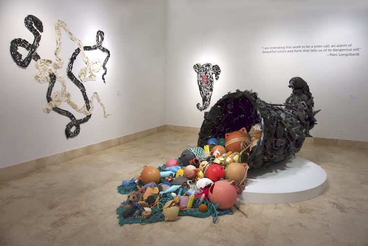Trois grandes installations d'art plastique, celle du centre une corne d'abondance renversant des objets en plastique sur le sol.