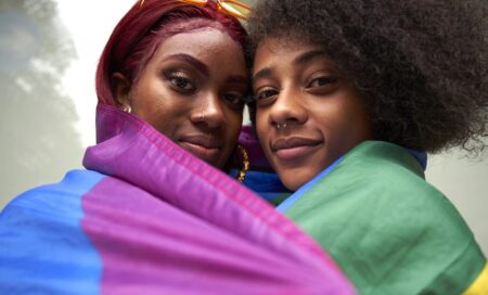 Two women draped in a rainbow Pride flag.