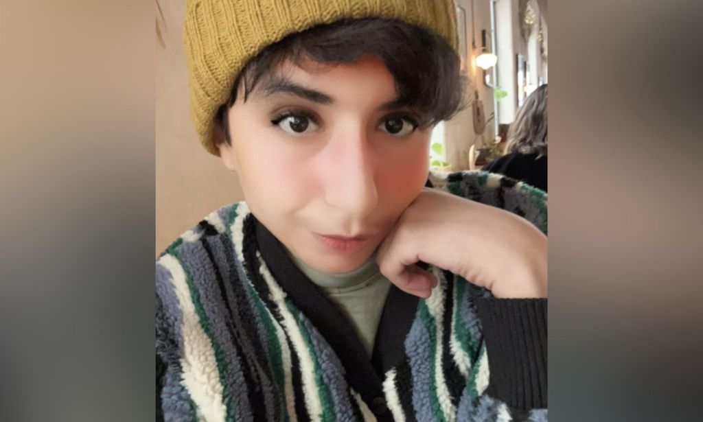 Eden Knight, une jeune femme trans saoudienne, porte un pull à rayures verticales en noir, crème et gris avec un bonnet jaune