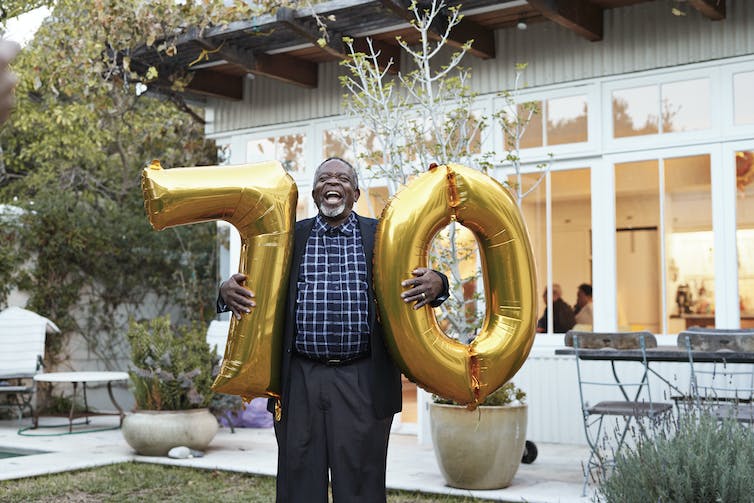 Adulte plus âgé tenant des ballons d'or du nombre 70 dans une arrière-cour