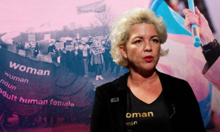 Posie Parker, also known as Kellie-Jay Keen-Minshull, in a black suit in front of a protest with a banner that reads 'woman, adult human female'.