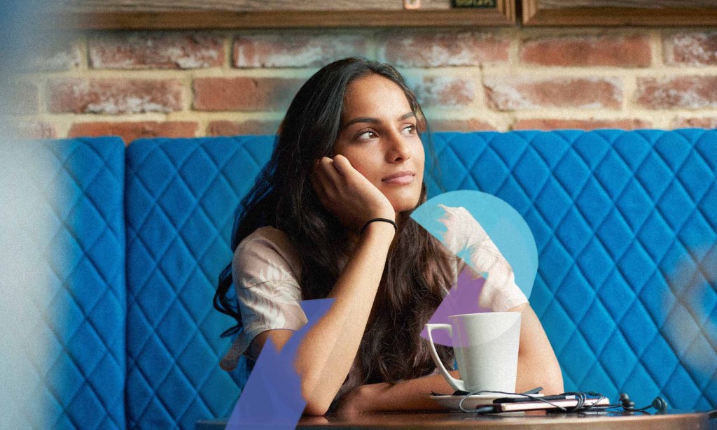 Une femme est assise, la tête sur la main, dans un café.