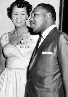 Une femme en robe de soirée avec un corsage se tient à côté d'un homme en costume, souriant et bavardant.