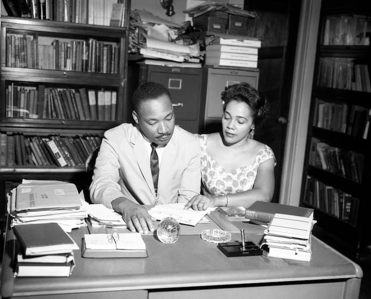 Un homme en costume clair et une femme en robe à manches courtes regardent ensemble une feuille de papier dans un bureau.