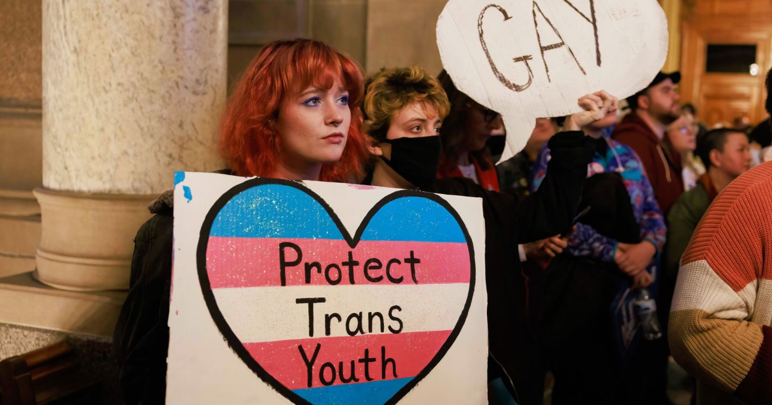 Les manifestants tiennent une pancarte indiquant "Protégez les jeunes trans" et "Gay" alors qu