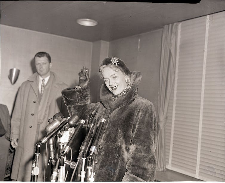 Christine Jorgensen debout devant un ensemble de microphones lors d'une conférence de presse