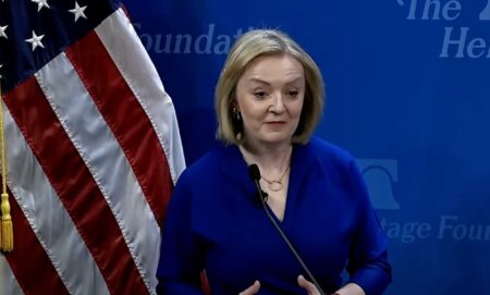 Liz Truss speaking in front of a US flag