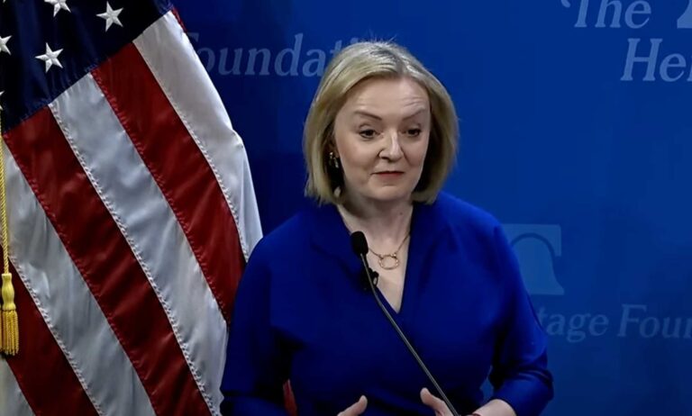 Liz Truss speaking in front of a US flag