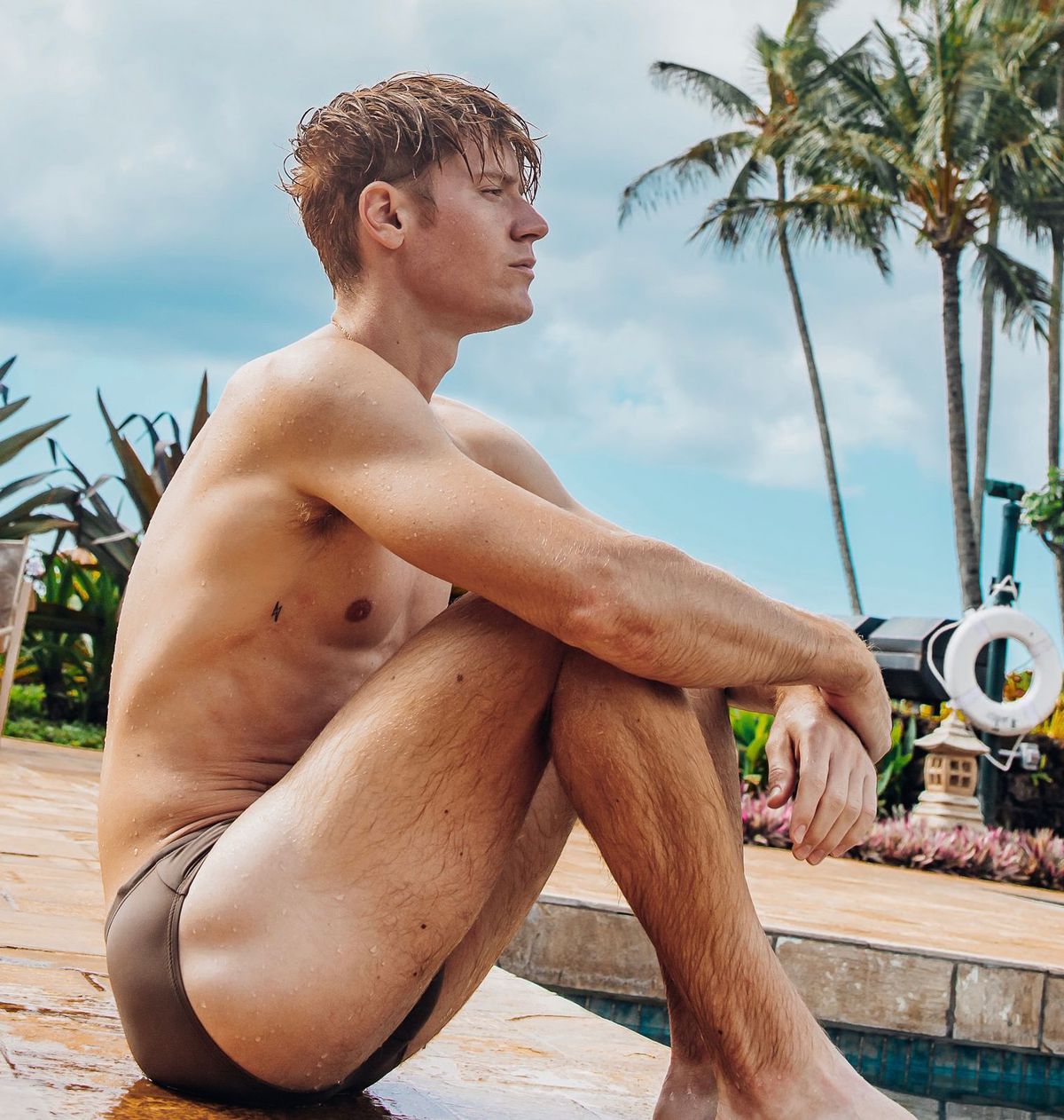 Zack Taylor est assis au bord d'une piscine en maillot de bain.