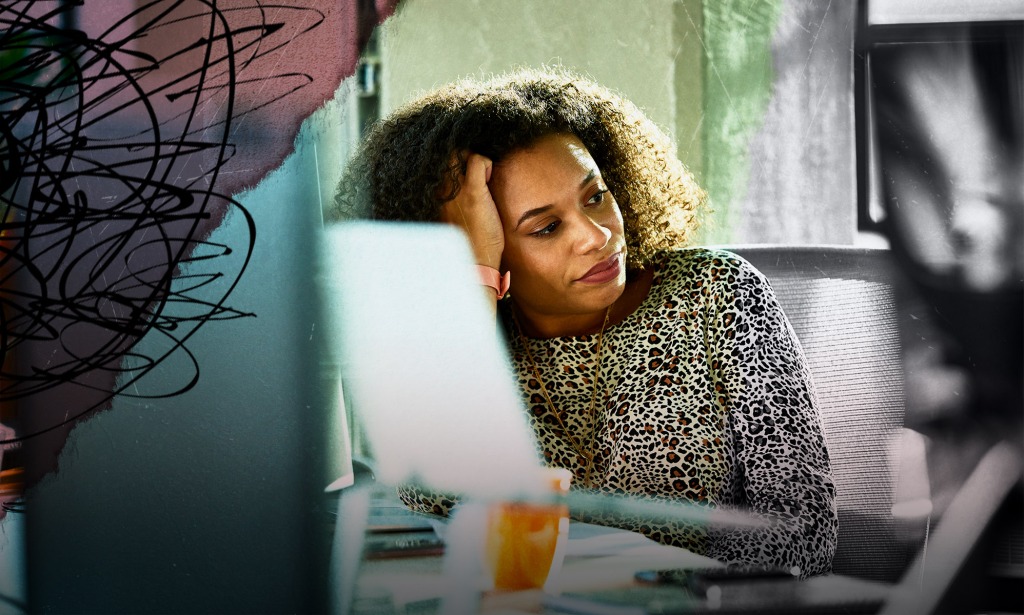 Une femme noire travaille à domicile.  Elle repose sa tête sur sa main droite.  Elle apparaît brûlée. 