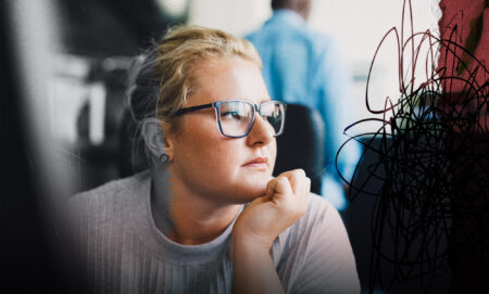 A female presenting person is looking out the window. They have eyeglasses on. They look stressed and there is a creative overlay for visual impact.