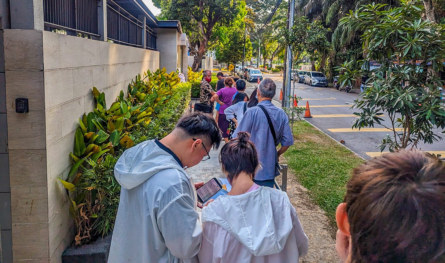 Des gens se sont alignés dans une rue verte bordée d'arbres devant le consulat de Thaïlande à Penang, en Malaisie. 