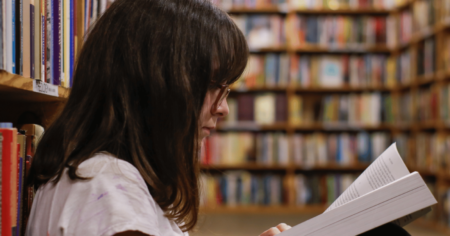 Un jeune lit un livre dans une bibliothèque scolaire comme réglage