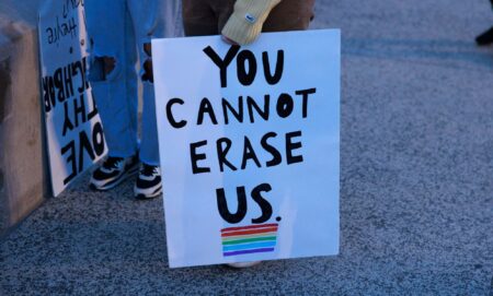 A person holds a sign reading 'You cannot erase us' with a rainbow LGBTQ+ flag below it during a protest against Republish's pushing 'Don't Say Gay or Trans' bills