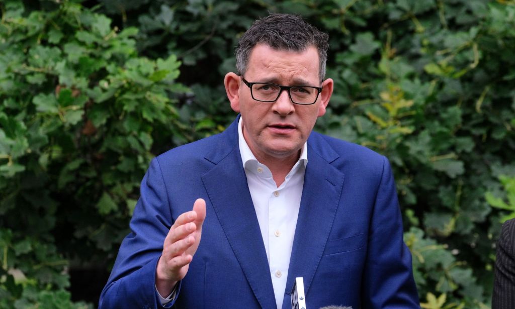 Dan Andrews, premier ministre de l'État australien de Victoria, porte une chemise blanche et une veste bleue alors qu'il se tient à l'extérieur et fait un geste d'une main