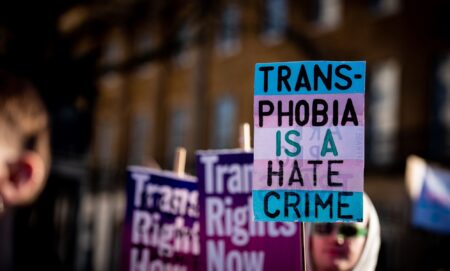 A person holds up a sign in the colours of the trans pride flag (blue, pink and white) reading 'Transphobia is a hate crime' during a protest