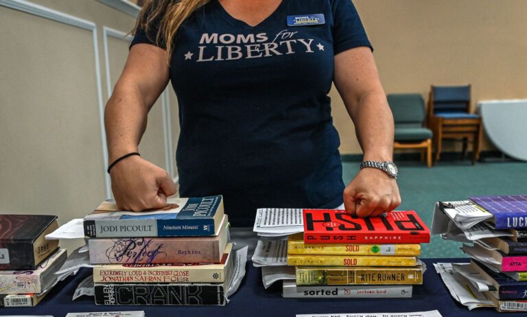 A member of Moms for Liberty rests her knuckles on the tops of a stack of books.