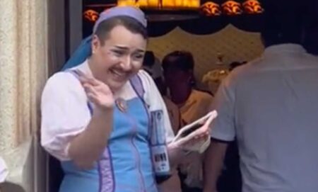 Disney employee Nick, a fairy godmother's apprentice, is a white person with a moustache wearing eye shadow and a blue dress