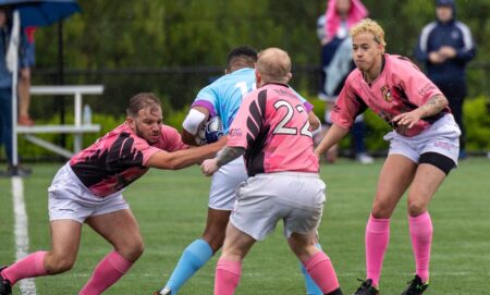 Trans rugby player Val Pizzo is mid tackle during an all-trans match in the US with various players wearing blue and pink jerseys